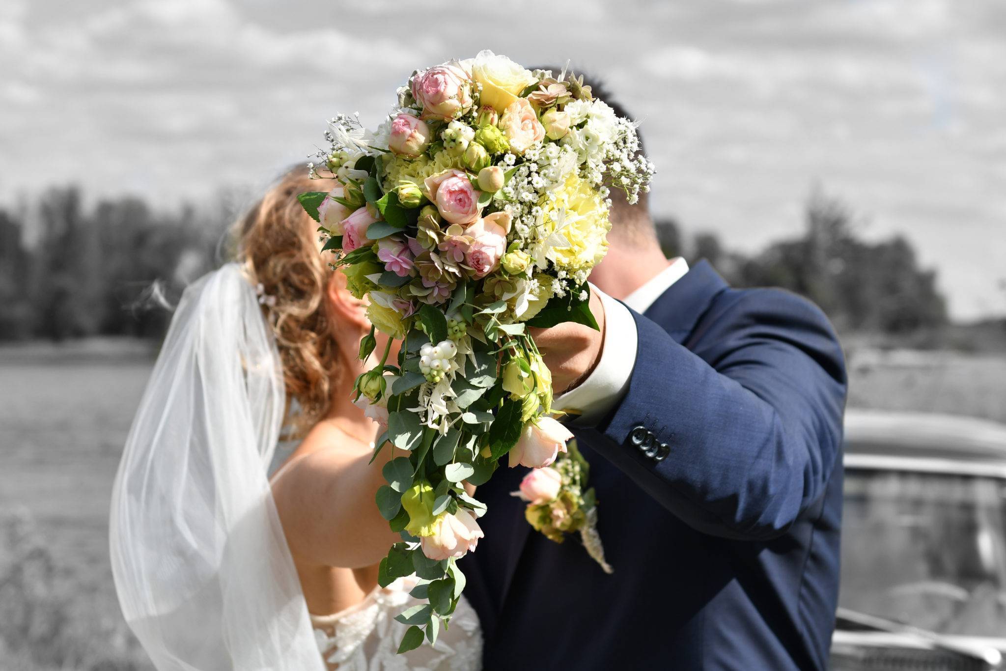 Brautpaarshooting mit entgengestrecktem schönem Brautstrauss in Farbe - der versteckte Kuss