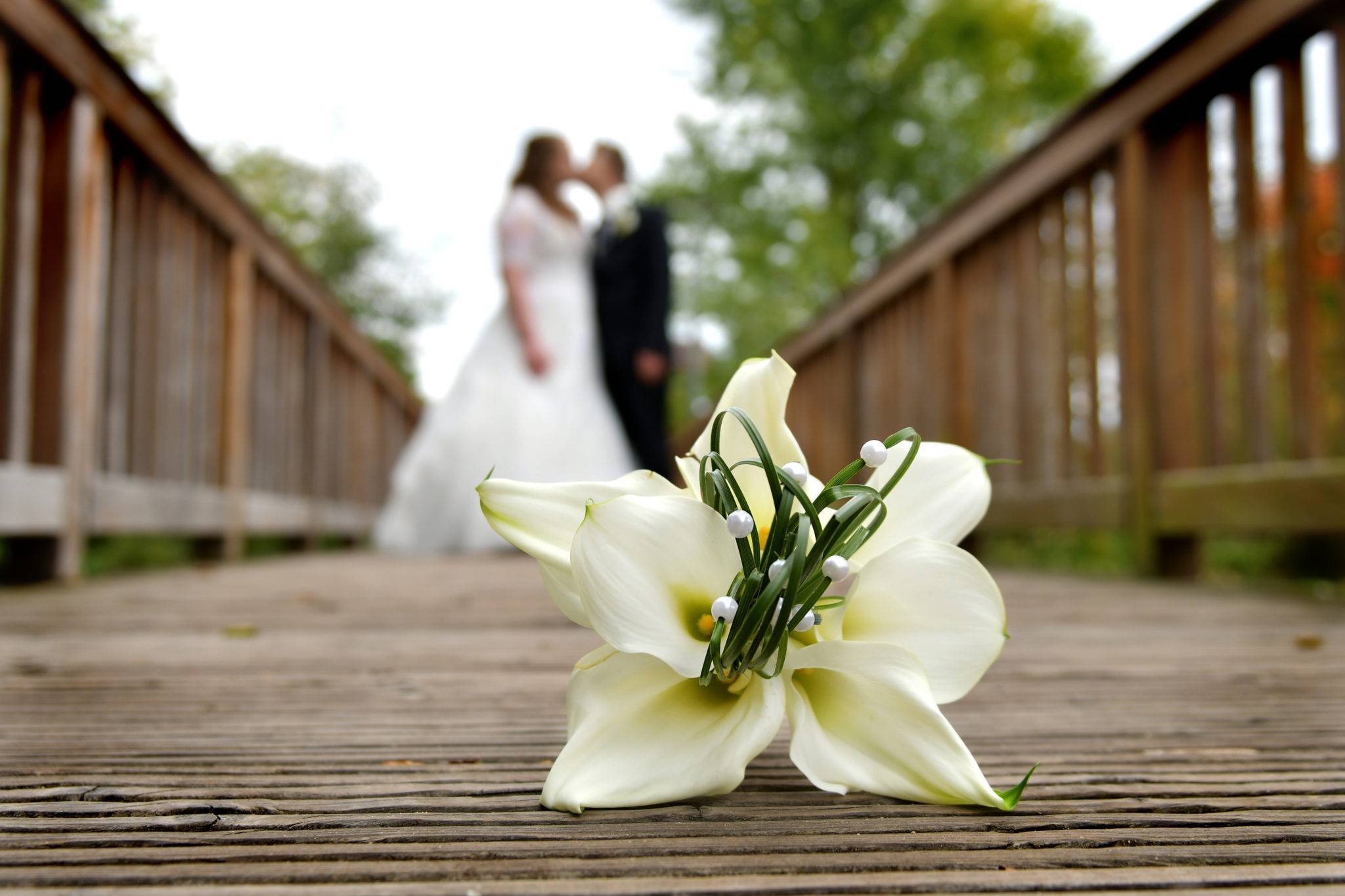 Brautpaarshooting auf einer Holzbrücke mit Kuss und Brautstrauss im Focus